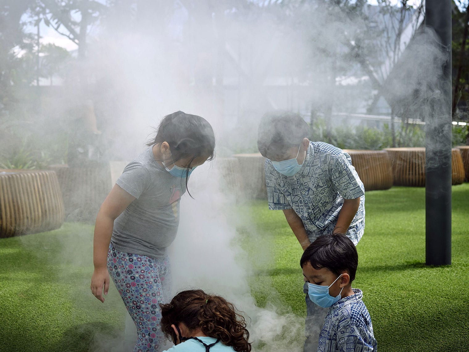 Four masked children stand on astroturf, looking at the ground and surrounded by mist