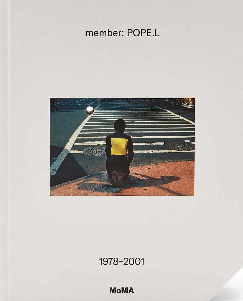 Book cover for the exhibition catalog "member: Pope.L." The cover is solid light-gray; at the center, a small color photo shows a man kneeling on the sidewalk in front of a crosswalk.