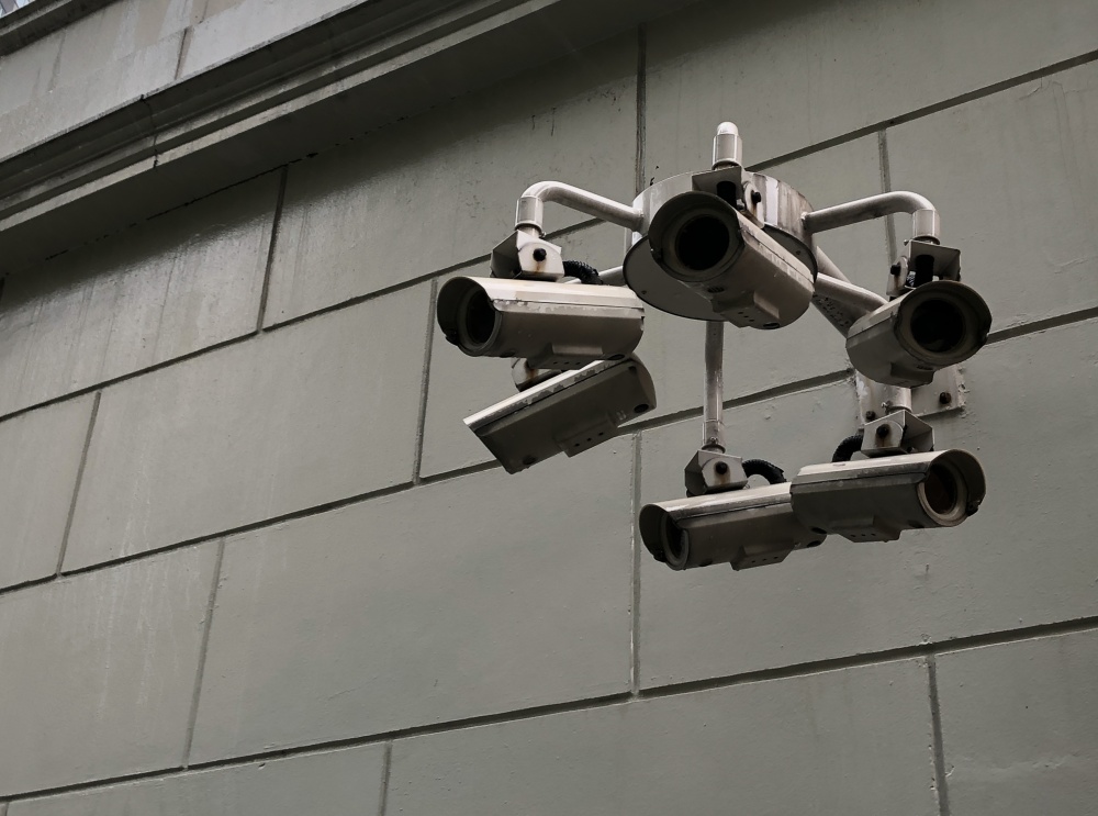 A gray tiled exterior wall mounted with an armature of six surveillance cameras.