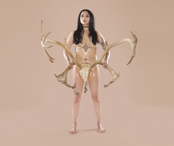Person with stereotypical female body holding skull of large deer in front of their genitals with an antler in each hand