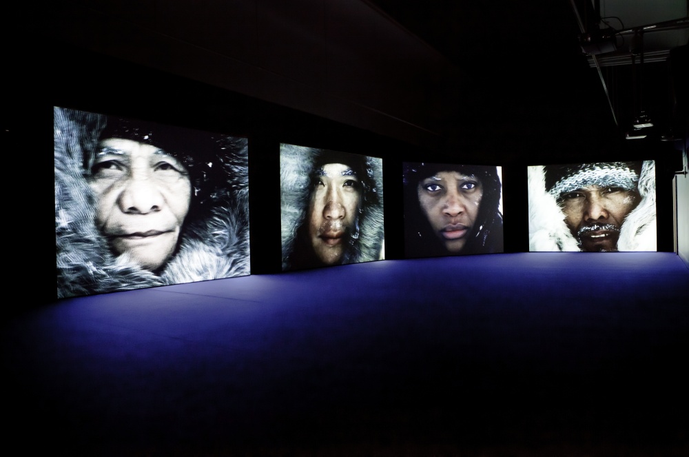 Projection of close-up portraits of actress Vanessa Myrie, representing Black explorer Matthew Henson, and three Inuit actors, representing the four Inuit men who accompanied Robert Peary and Matthew Henson on their voyage to the North Pole