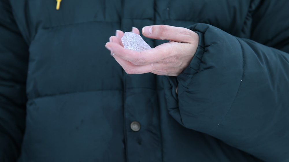 Close-up photograph of a bare hand holding an ice cube