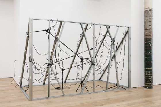 An art installation constructed of vertical metal studs and mic stands, intertwined with black electrical cables