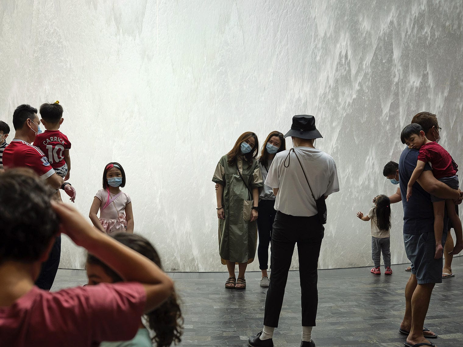 Several masked people stand, look, and take pictures in front of a wall of water