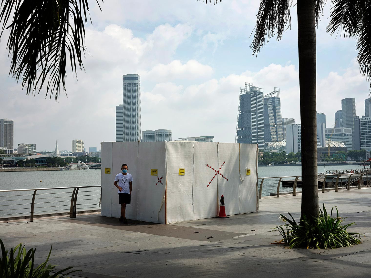 A lone masked person stands before a taped-off small building by the water in Singapore