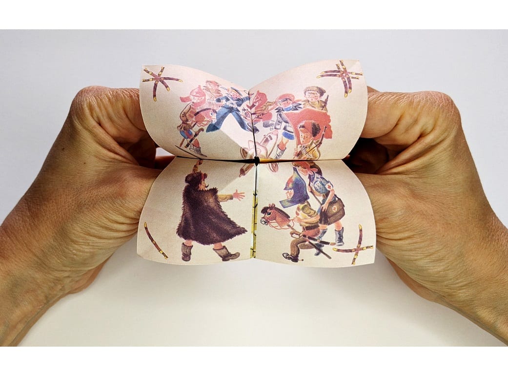 Alt text: Color photograph of two hands holding an interactive sculpture made of folded paper in the shape of a child's "fortune teller" game.