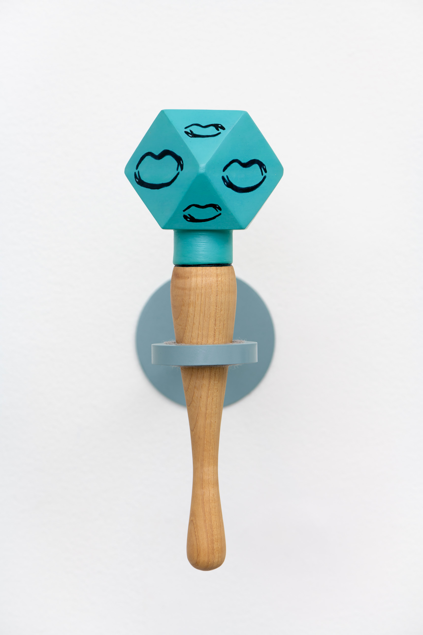 A blue, multifaceted ceramic rattle with a wooden handle. Each facet is decorated with a line drawing of two snakes laid flat in the shape of a mouth.