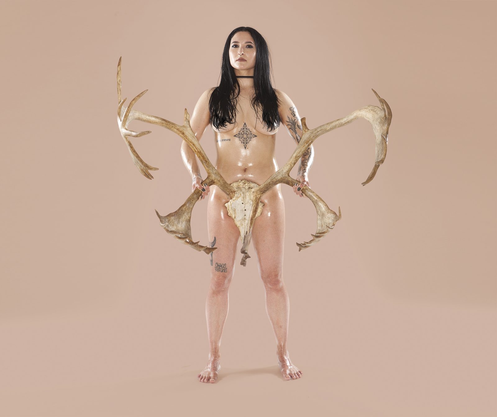 Person with stereotypical female body holding skull of large deer in front of their genitals with an antler in each hand