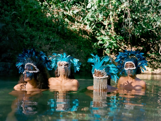 Four figures inside a river from the shoulder down, with blue masks covering their faces.